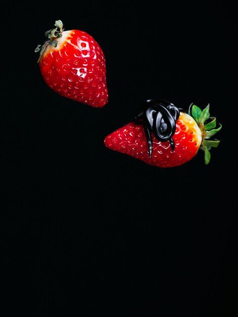 Dos fresas maduras rojas en chocolate sobre un fondo negro cayendo