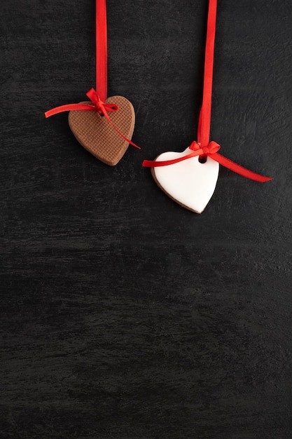 Dos galletas con forma de corazón de pan de jengibre cuelgan de una cinta roja. Fondo negro, copie el espacio. Día de la Madre. Día de San Valentín.