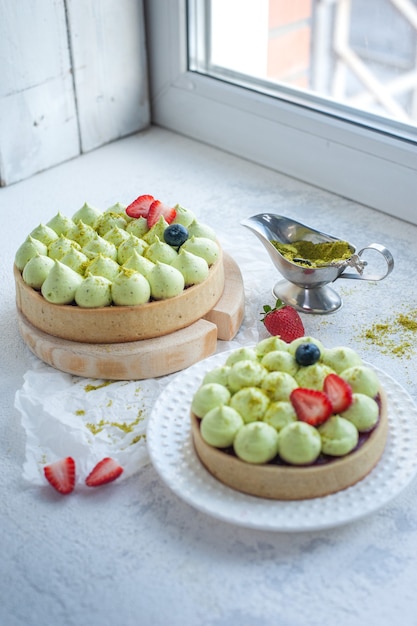 Foto dos galletas de mantequilla redondas con crema de pistacho verde y mermelada de fresa junto a la ventana
