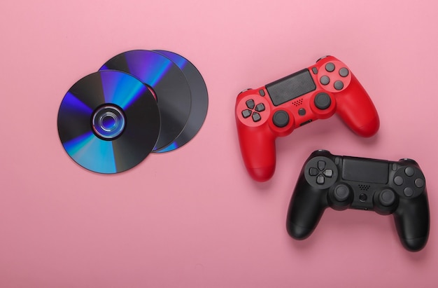 Dos gamepads y discos compactos cd sobre un rosa pastel