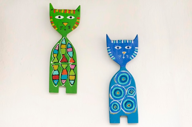 Dos gatos azules y verdes de madera con patrones en una pared de piedra blanca