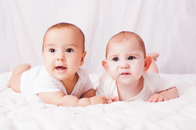 Foto dos gemelos bebés acostados boca abajo en la sábana blanca