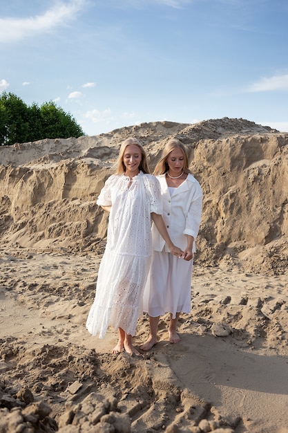 Dos gemelos bonitos jóvenes con cabello largo y rubio posando en la cantera de arena con elegante vestido blanco, falda, chaqueta.