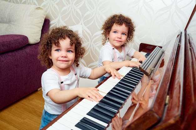 Dos gemelos divertidos tocando el piano juntos sonriendo riendo niños aprenden a tocar el piano el concepto de formación de niños