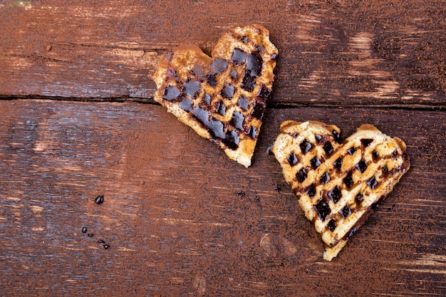 Dos gofres belgas en forma de corazón con chocolate en madera