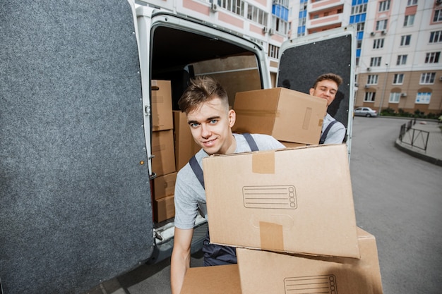 Dos guapos trabajadores uniformados están descargando la camioneta llena de cajas