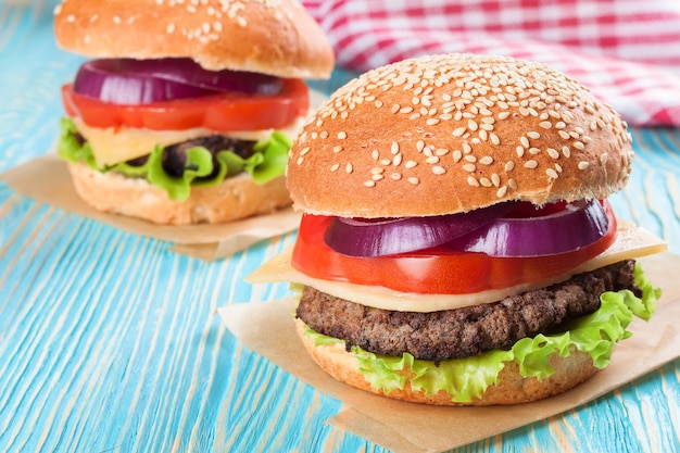 Dos hamburguesas caseras con queso con empanadas de carne y ensalada fresca en bollos de mar, sered sobre mesa de madera azul.