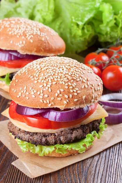 Dos hamburguesas caseras con queso con empanadas de carne, ensalada fresca, tomates y cebolla en bollos de mar, servidos en una mesa de madera marrón.