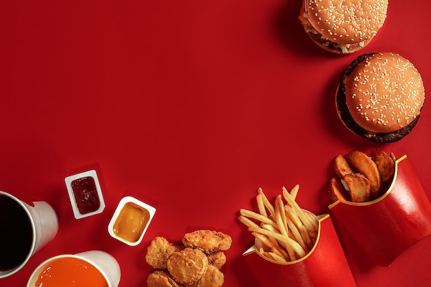 Dos hamburguesas y papas fritas, salsas y bebidas sobre fondo rojo, comida rápida, vista superior, endecha plana con ...