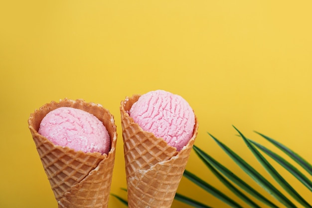 Dos helados de fresa en cono sobre un fondo amarillo. Hoja tropical. Foto de verano