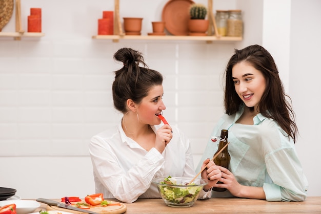 Dos hembras jóvenes seductoras haciendo ensalada en la cocina