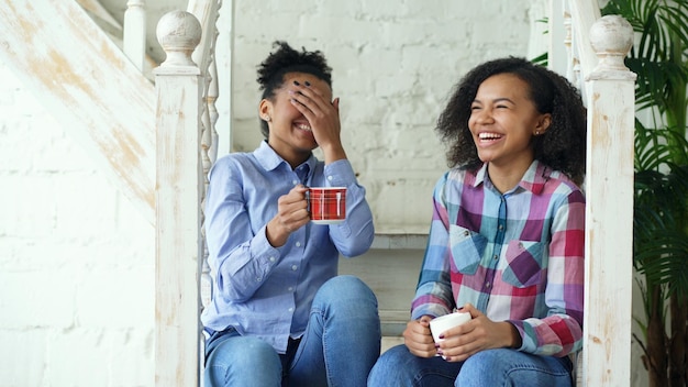 Dos hermanas afroamericanas rizadas sentadas en las escaleras se divierten riendo y charlando juntas