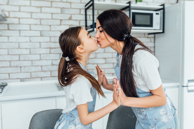 Foto dos hermanas bonitas se besan al hacer pasteles en la cocina