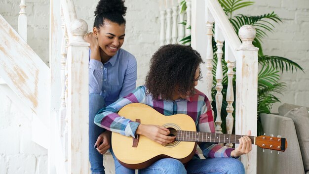 Dos hermanas brasileñas rizadas sentadas en las escaleras y practican para tocar la guitarra acústica