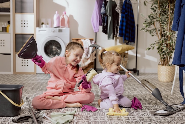 Dos hermanas dulces niñas limpian el piso de la lavandería Los niños juegan mientras hacen las tareas del hogar barriendo la ropa en el baño