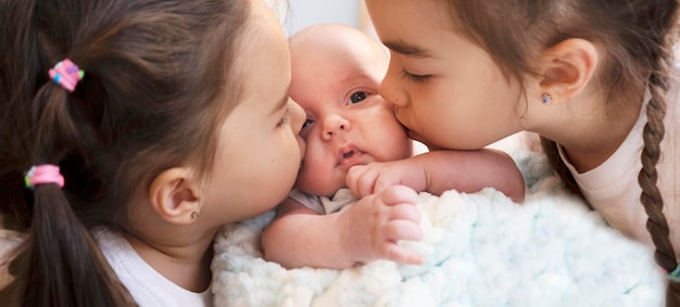 Foto dos hermanas encantadoras besan a su hermano pequeño recién nacido niño con niñas hermanos felices