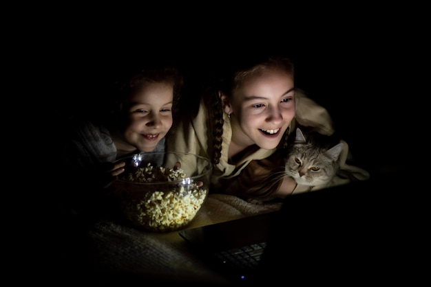 Foto dos hermanas con un gato ven dibujos animados en el dispositivo y se divierten juntas