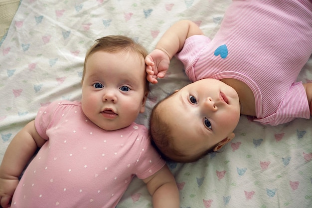 Foto dos hermanas gemelas bebé en ropa rosa acostado en la cama en un pañal