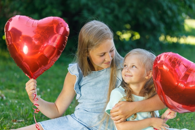 Dos hermanas con un globo en forma de corazón en la naturaleza.