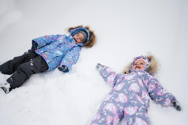 Dos hermanas haciendo ángel de nieve mientras yacen en la nieve