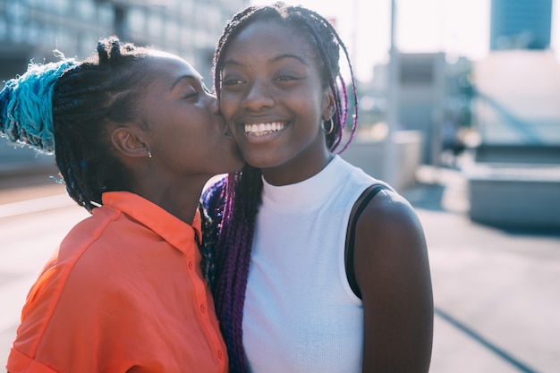 Dos hermanas hermanas al aire libre sonriendo besándose en la mejilla