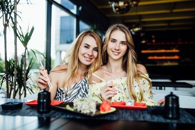 Dos hermanas jóvenes y bastante rubias tienen un tiempo de sushi en un café moderno, pasan tiempo juntos