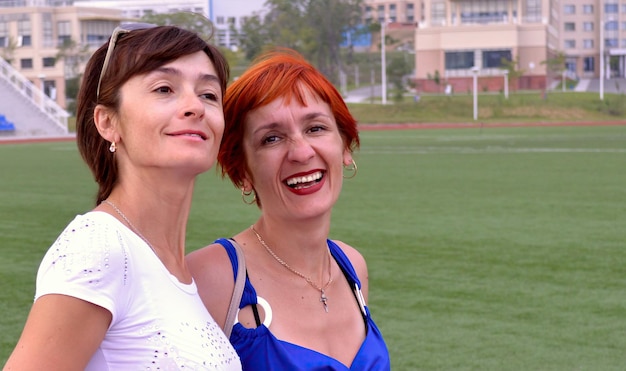 Dos hermanas jóvenes felices riéndose sinceramente del campo de fútbol durante el entrenamiento de fútbol en la suma