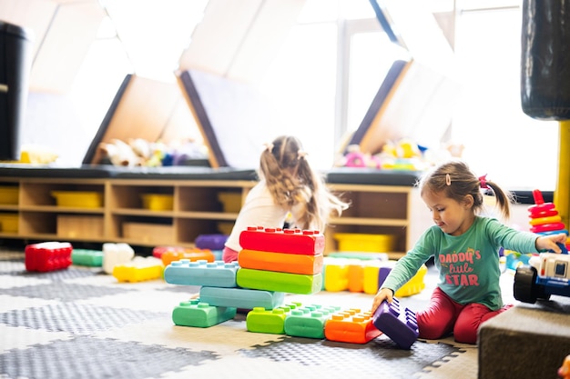 Dos hermanas jugando en el centro de juegos para niños mientras construyen con bloques de plástico de colores