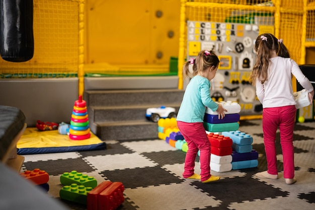 Dos hermanas jugando en el centro de juegos para niños mientras construyen con bloques de plástico de colores