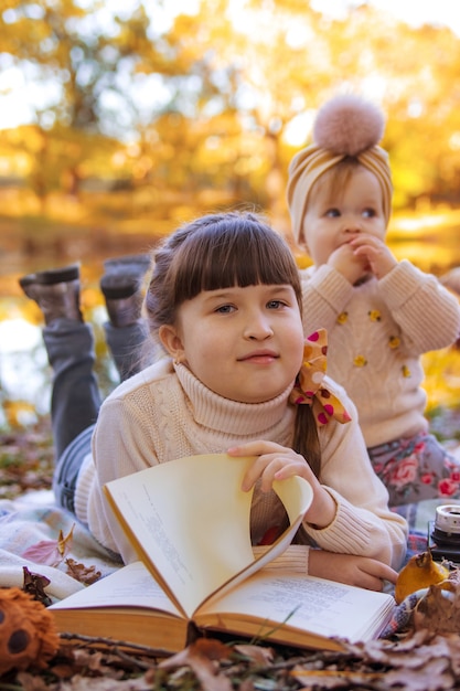 dos hermanas jugando en el parque de otoño con un libro