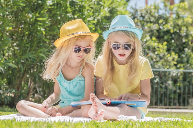 Dos hermanas leyendo un libro de interés en el jardín, diversión veraniega