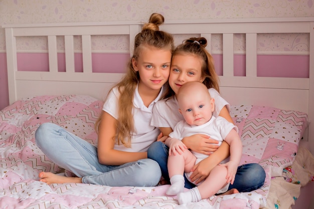 Foto dos hermanas mayores sostienen a un bebé en sus brazos