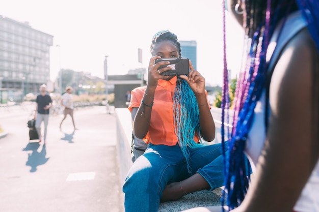 Dos hermanas de mujeres al aire libre usando teléfono inteligente tomando fotos