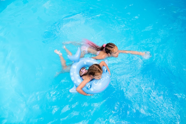 Dos hermanas nadan en una piscina con agua azul y tienen un ventilador Vacaciones familiares de verano