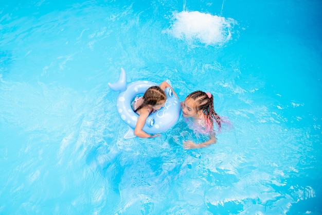 Dos hermanas nadan en una piscina con agua azul. El verano. Vacaciones familiares.