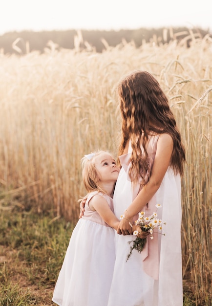Dos hermanas de niñas se abrazan y recogen flores en el verano