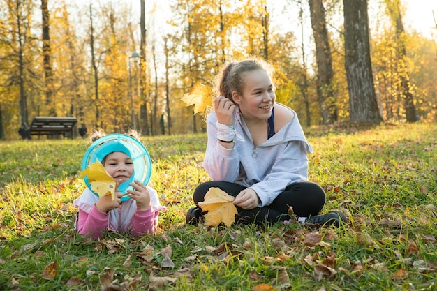 Dos hermanas en el parque de otoño, una niña tendida en el suelo y otra sentada a su lado