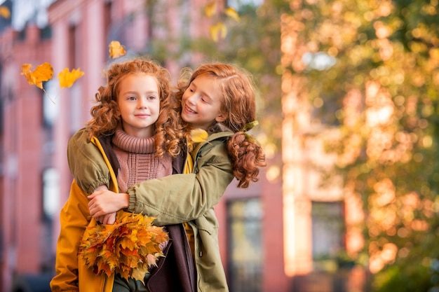 Dos hermanas pelirrojas caminan alegremente por la calle de la ciudad durante la caída dorada de la hoja de otoño