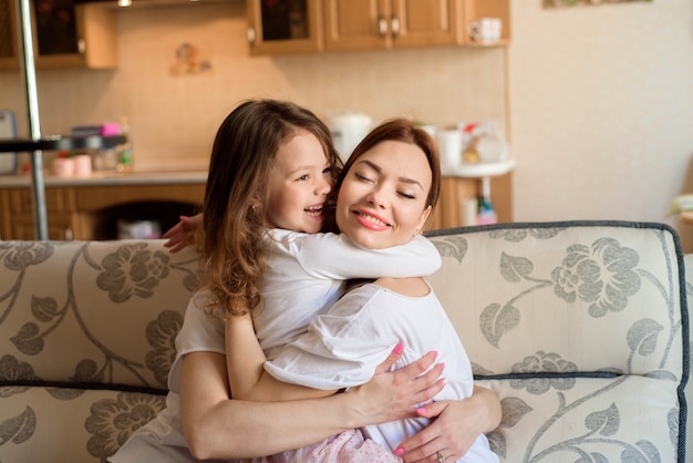 Dos hermanas y pequeña hija que sonríen y que abrazan en el fondo interior del hogar.