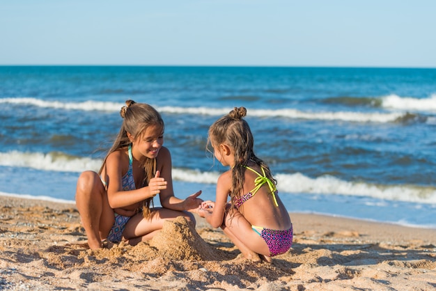 Dos hermanas pequeñas están construyendo castillos de arena