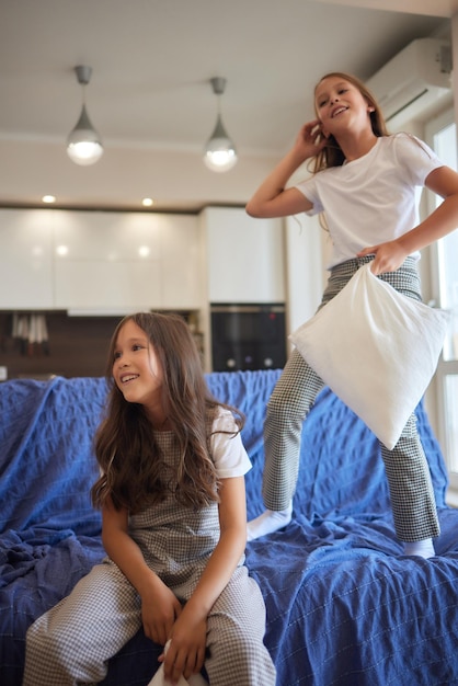 Foto dos hermanas con pijamas blancos pelean con almohadas y se divierten con el concepto de bienestar y curación de los jóvenes