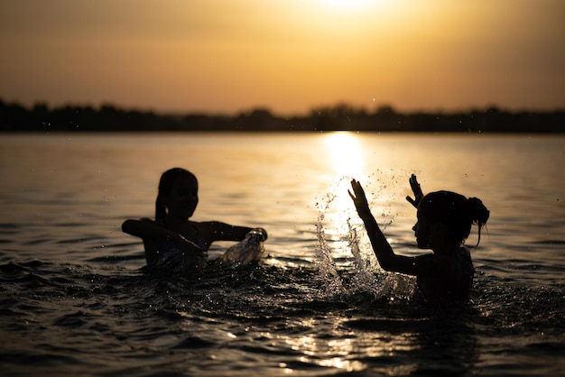 Dos hermanas salpicaduras de agua jugando en el lago al fondo del atardecer