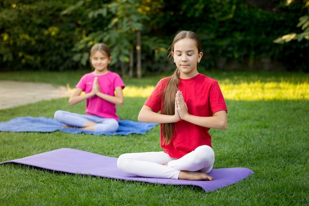 Foto dos hermanas sonrientes practicando yoga sobre el césped en el parque soleado