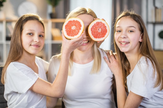 Dos hermanas sosteniendo rodajas de pomelo cerca de los ojos de la madre