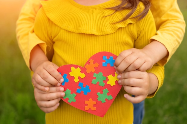 dos hermanas sostienen un corazón rojo con coloridos rompecabezas en el interior hechos con sus propias manos