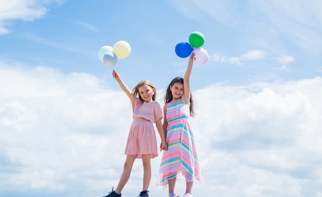 Dos hermanas sostienen un globo de fiesta. infancia feliz. vacaciones de verano. las niñas pequeñas se abrazan. amor y apoyo. concepto de hermandad y amistad. tiempo de unión familiar. mejores amigos con globo.