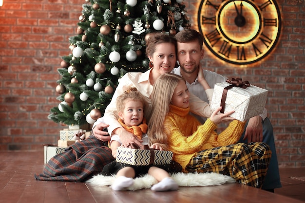 Dos hermanas y sus padres sentados cerca del árbol de Navidad