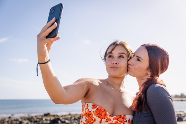 Dos hermanas se toman una selfie en la playa y una le da un beso a la otra en la mejilla