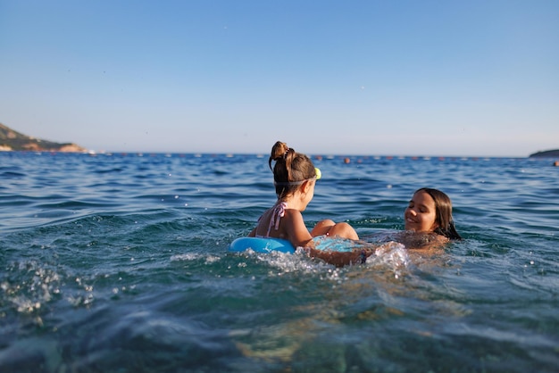 Dos hermanas en trajes de baño juegan con un anillo inflable en el mar