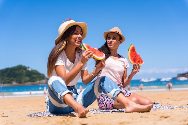 Dos hermanas en verano en la playa comiendo una sandía de vacaciones con el mar de fondo